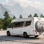 Housse de vélo pour camping-car : guide pratique pour bien la choisir Camping-car stationné sur une aire de montagne, avec deux vélos recouverts d’une housse ajustée sur le porte-vélos arrière, dans une lumière naturelle réaliste.