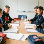 Quel recours choisir pour suspendre le refus préfectoral d’un agrément de sécurité civile ? Une équipe mixte de bénévoles de la sécurité civile française réunie autour d’une table avec des dossiers administratifs vierges et du matériel discret de premiers secours dans une salle de réunion.